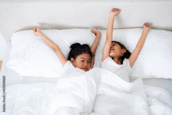 Fototapeta Two cute asian children waking up and stretching in bed