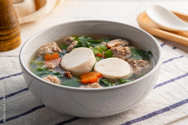 Fototapeta Clear Ivy gourd soup with minced pork and soybean tofu in white bowl on wooden table,Thai food.(gaeng jued tum luang)