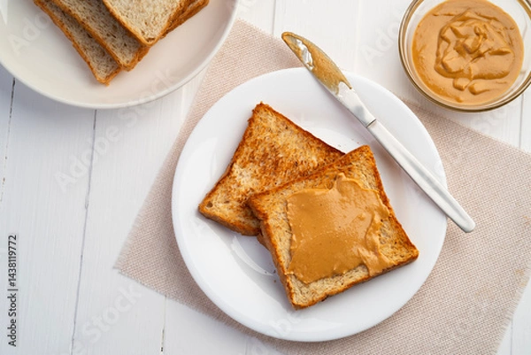 Fototapeta Toast bread and Homemade peanut butter.Spreading peanut butter on slice whole wheat bread in white plate.Top view