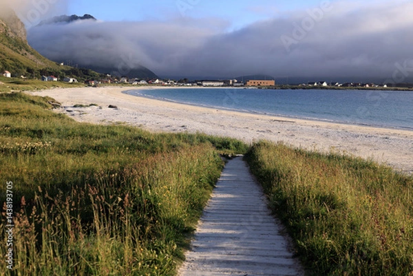 Fototapeta Landscape photo with a view of mountains partially covered by clouds and Ramberg Beach late in the evening during the "white nights" in the Lofoten Islands in Norway