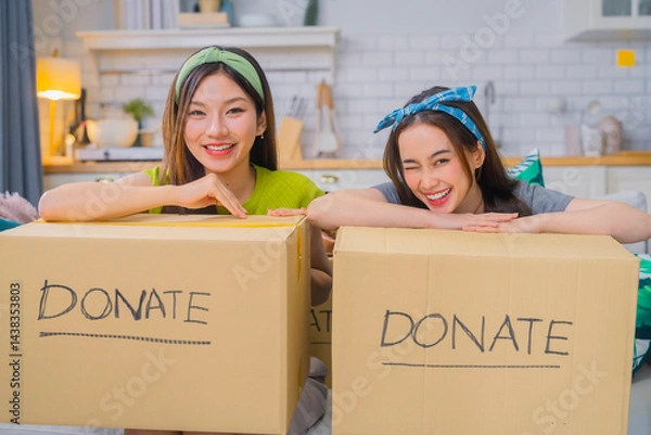Obraz asian woman friend An Organizing clothes with friends, preparing to donate items, and enjoying productive day together Taking checking clothes packed in a cardboard boxes for donation
