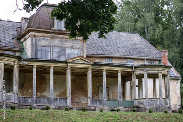 Fototapeta 
A run-down manor house with columns and a gray roof, set on a green lawn with trees in the background.