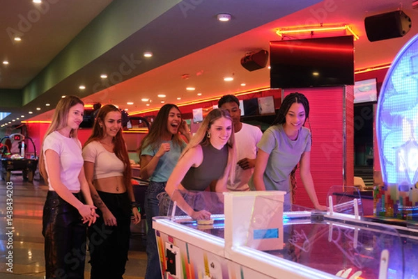 Obraz Group of young people enjoying a game of air hockey in vibrant arcade