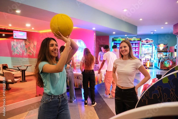 Obraz Two friends playing arcade basketball with other young people having fun in the background
