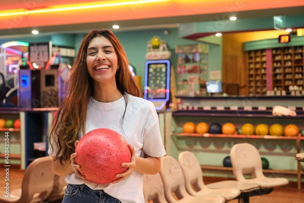 Obraz Happy young woman holding a bowling ball and smiling in a bowling alley