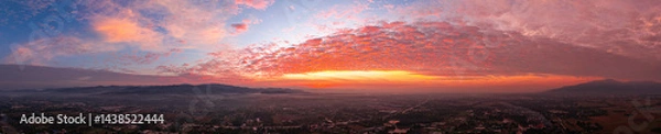 Fototapeta Aerial shot of a gorgeous sunrise. A panoramic view of dramatic mountain peaks silhouetted against a vibrant sunset sky, with fiery hues of red, orange, and pink blending into the fading blue.