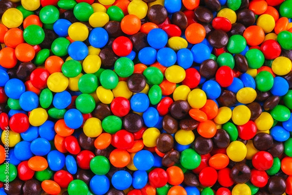 Fototapeta Colorful candy-coated chocolates in a vibrant, playful pile. Bright red, blue, yellow, green, and orange sweets create a cheerful, festive background perfect for parties, designs, and advertisements.