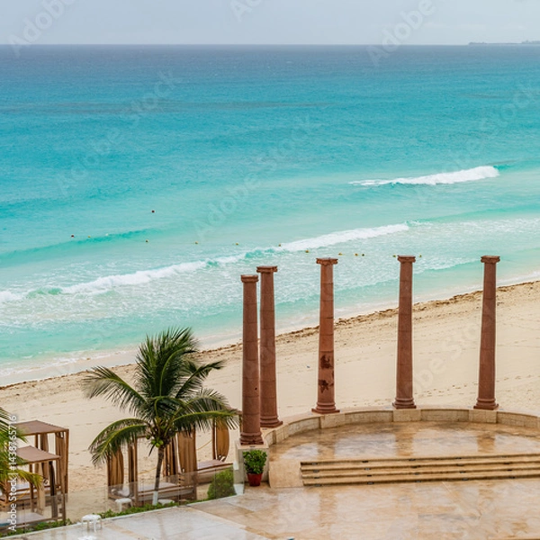 Fototapeta Empty Cancun beach with turquoise waters, palm trees, and ancient-style columns under a rainy morning sky. High-quality photo . Cancun Hotel Zone, Mexico
