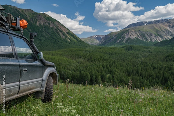 Fototapeta An off-road family car is parked in a green meadow overlooking a forest and a mountain gorge. Mud wheels for an SUV on a background of green vegetation. A family car for traveling.