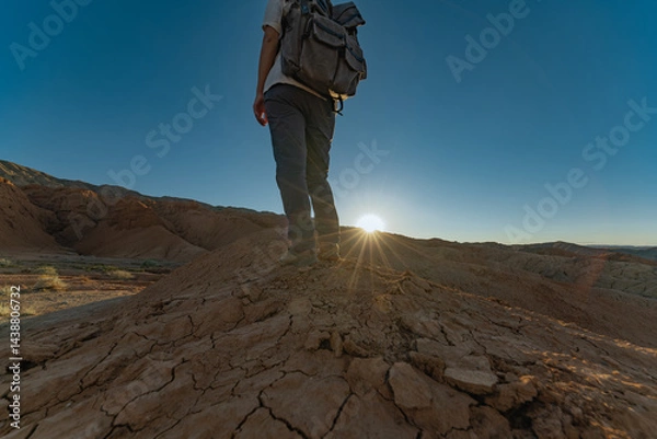 Fototapeta The traveler stands on a hill during the golden hour, when the sun is almost below the horizon. A man with a backpack, a photo from the back, at sunset.