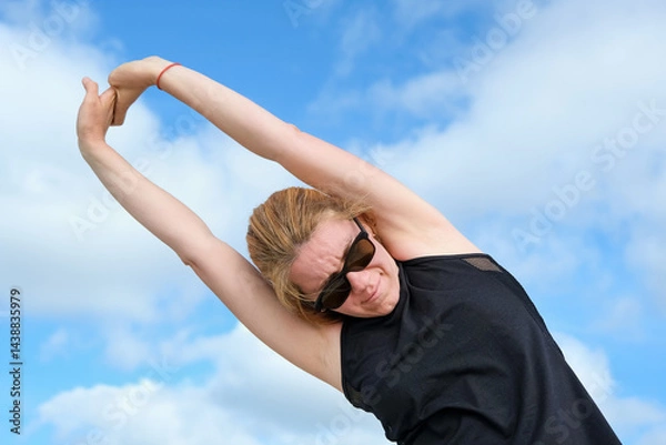 Obraz Woman stretching arms overhead outdoors under bright sky, enjoying fitness and wellness routine, focusing on flexibility, strength, and energy in a natural environment