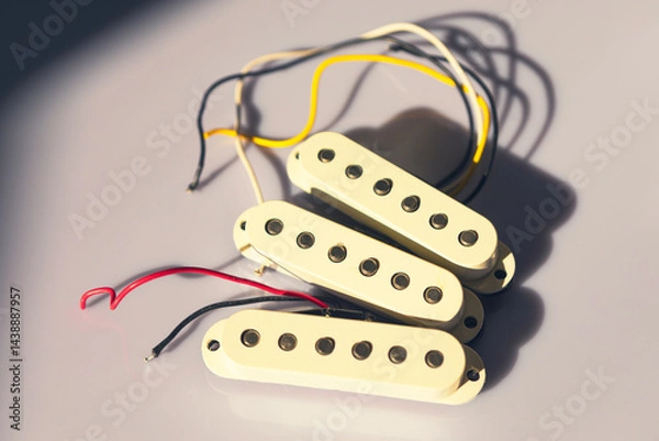 Fototapeta Single-coil guitar pickups with cream-colored covers and visible pole pieces are placed on light surface, casting shadows. Wires extend from each pickup, indicating they are ready for installation