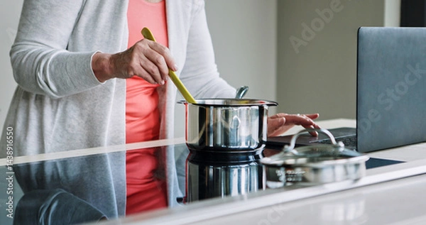 Fototapeta Woman, hands and cooking on stove with laptop, recipe and reading a blog about food. Kitchen, pot or person mixing with wood spoon, scroll online or learning to prepare meal or dinner with nutrition