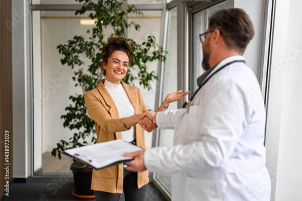 Fototapeta Male doctor in lab coat shaking hands with female patient while standing in hospital during medical visit