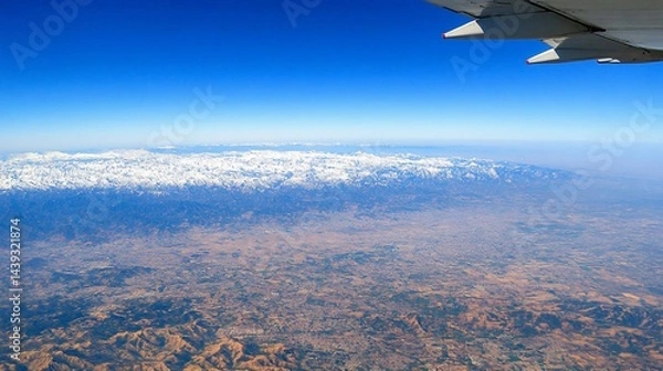 Fototapeta Aerial view of snow-capped mountains and vast landscape from airplane window