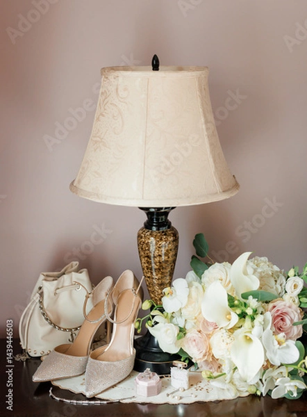 Obraz Bride's wedding accessories in her room near table lamp close up. Bride's bouquet of white flowers, high heels shoes, handbag, wedding rings and perfume prepared for the wedding day