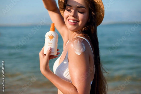 Fototapeta Woman applying sunscreen on her shoulder while enjoying a sunny day at the beach, promoting skin protection and healthy habits, summer skincare concept.