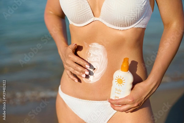 Fototapeta Woman applies sunscreen on her skin at the beach, enjoying the sun while emphasizing the importance of skin protection and sun safety for health.