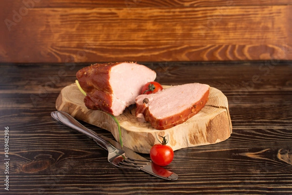 Obraz two pieces of fresh processed meat, carbonate and pastrami in a package, cutlery and cherry tomatoes in close-up on a dark wooden background