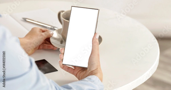 Fototapeta Female hands holding blank screen mobile phone on white desk with credit card, coffee and pen. Empty display, screen ready for branding. Modern technology, online activities and shopping concept.