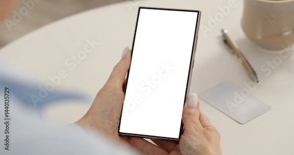 Fototapeta Close-up of woman hands and blank screen mobile phone on white desktop background. Empty display, screen ready for branding. Modern technology usage, online activities and digital marketing concept.