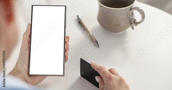 Fototapeta Female hands holding blank screen mobile phone and  credit card on white desk with coffee and pen. Empty display, screen ready for branding. Modern technology, online activities and shopping concept.