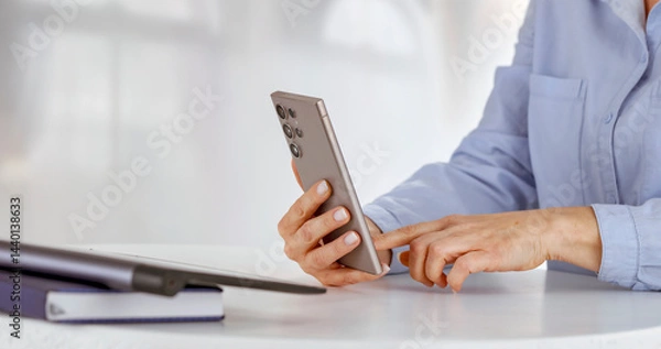 Fototapeta Close-up of woman holding a phone in one hand and with the other scrolling browsing websites and shopping online in the office or home setting. Modern technology and convenience of online shopping.