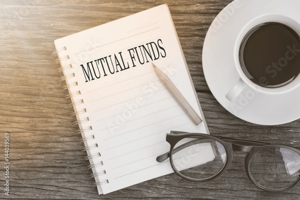Fototapeta Concept MUTUAL FUNDS message on notebook with glasses, pencil and coffee cup on wooden table.