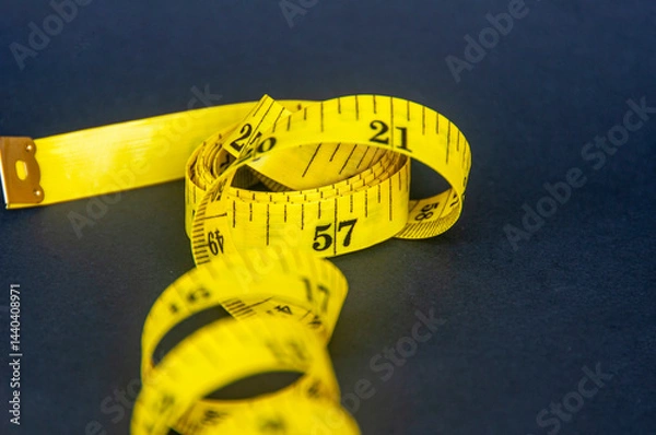 Obraz Close up view of yellow measure tape on dark background with customizable space for text. Dieting and copy space concept