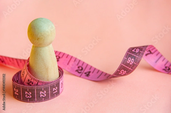 Fototapeta Pink measure tape wrapping a wooden doll with customizable space for text. Diet and copy space concept