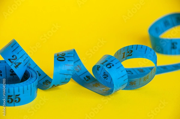 Fototapeta Blue tape measure on yellow background with customizable space for text. Dieting concept