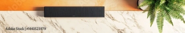 Fototapeta A flat lay of a black soundbar on a white marble countertop, with an orange and beige border
