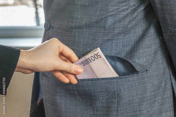 Obraz Hand drops European currency banknotes into the pocket of a man in a suit and tie standing in front of him. To give a bribe. Corruption