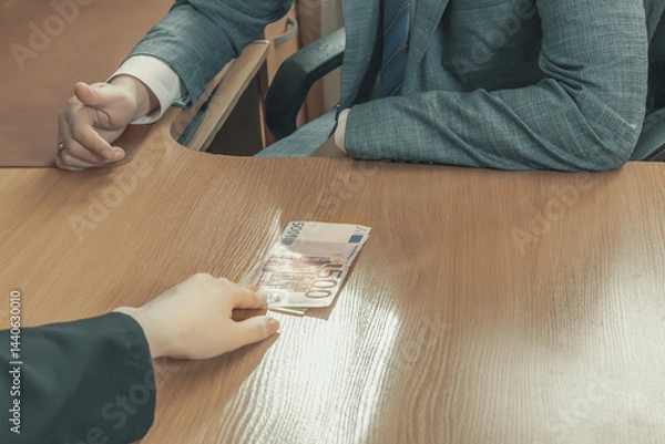 Obraz Hand moves euro bills across an office table towards a man in a suit and tie sitting opposite. Give a bribe. Corruption