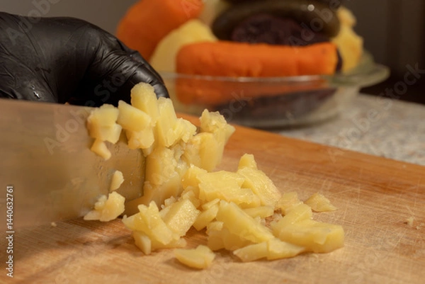 Obraz Chef cutting boiled potatoes for salad on a cutting board against the background of other vegetables. Close-up. Cooking