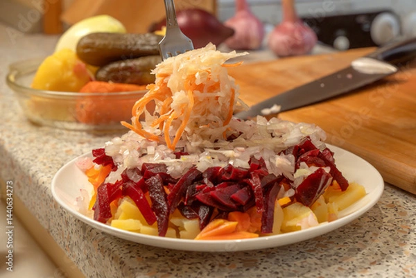 Obraz Chef adding sauerkraut to chopped onions and boiled beets, potatoes and carrots to prepare vinaigrette salad. Close-up. Food preparation