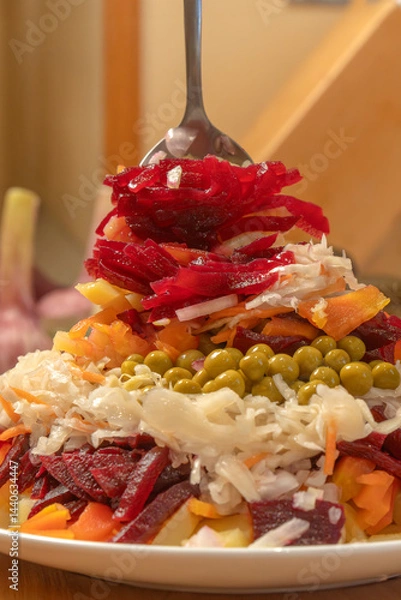 Obraz Chef stirs with a spoon a salad of boiled vegetables - beets, potatoes and carrots, green peas, onions, fermented cabbage and cucumbers before serving. Vinaigrette. Healthy eating. Close-up