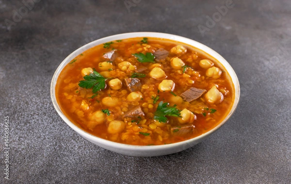 Obraz Bowl of Moroccan harira soup with chickpeas, beef, lentils and fresh parsley on grey background. Middle East cuisine.