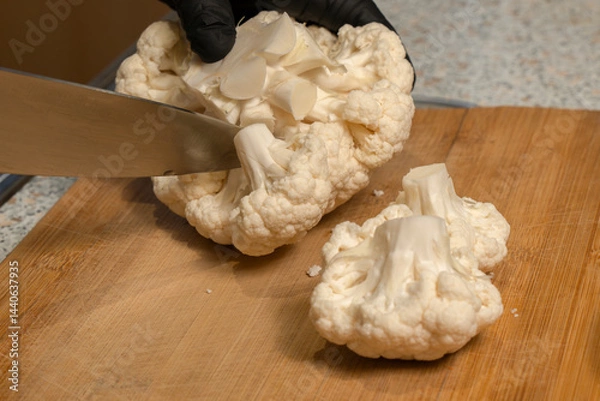 Obraz Chef divides a head of cauliflower into florets on a kitchen cutting board. Close-up