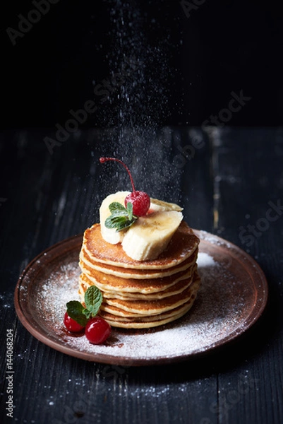 Fototapeta American pancakes on a plate with banana, cherry, mint and powdered sugar. Dark background. Vertical shot