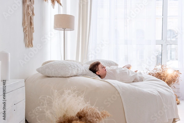 Fototapeta Cheerful little girl is having fun playing and hiding under a blanket on a comfortable bed in a cozy and bright bedroom, enjoying her playtime with laughter and excitement