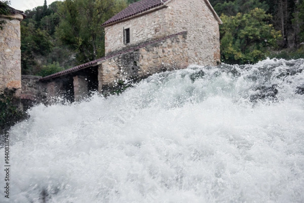 Fototapeta White water cascading over the rocks under old stone watermills in the lush Krka national park, Croatia, creating a picturesque scene of nature and history
