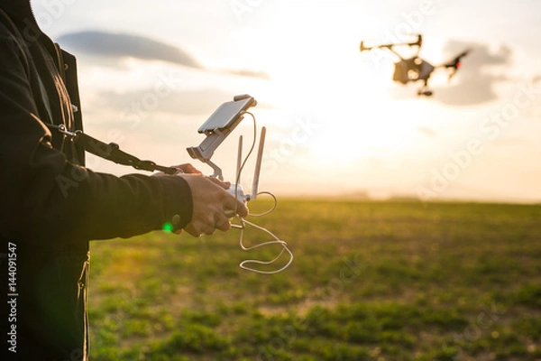 Fototapeta Man operating a drone with remote control. Dark silhouette against colorful sunset.