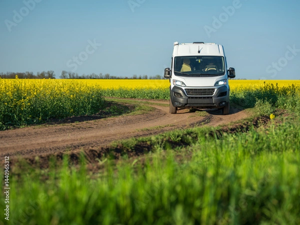 Obraz view to white commercial minibus on farm road between rapeseed fields in spring day