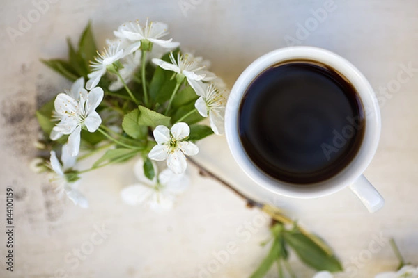 Fototapeta Cup of black coffee on a light colored wooden tray together with cherry twig in a bloom, view from above