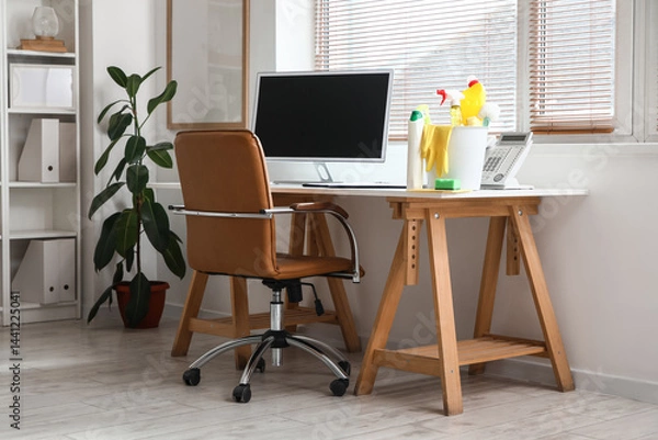 Fototapeta Plastic bucket with cleaning supplies and computer on table in modern office