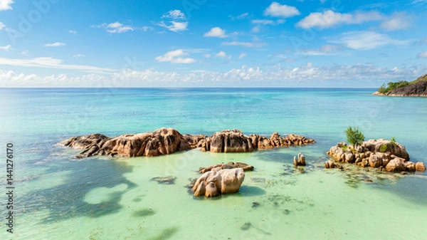 Fototapeta Massive granite rocks rest in shallow, turquoise waters, blending into the tropical landscape.