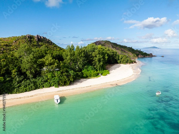 Fototapeta A tranquil white sand beach bordered by vibrant green trees, meeting the gentle turquoise waters of a serene bay. Curieuse, Seychelles.