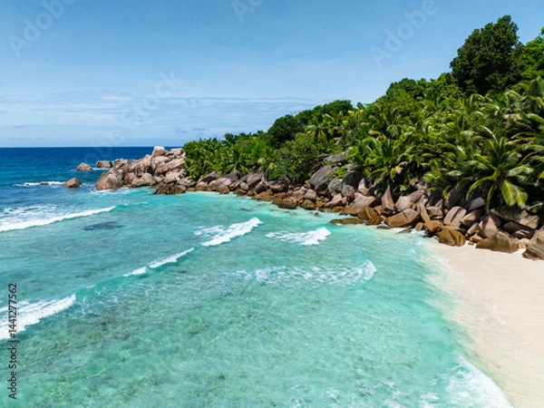 Fototapeta Turquoise waters meeting lush green vegetation and rocky coastline, offering a serene view. Seychelles, La Digue.