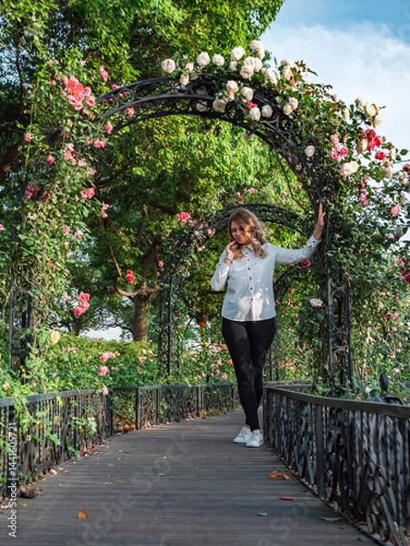 Fototapeta Young woman enjoying a serene moment in a flower-adorned archway in a lush garden during daylight hours